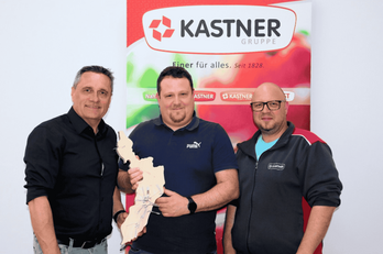 Drei Personen welche vor einem KASTNER Roll-up  stehen. Die Person in der Mitte hält ein sehr großes Puzzleteil in der Hand.