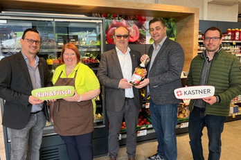 Fünf Personen welche vor einer Kühlvitrine stehen. Drei Personen halten Logo Schilder von "Nah&Frisch" sowie von "KASTNER Gruppe". Die anderen zwei Personen halten eine Schaumweinflasche.